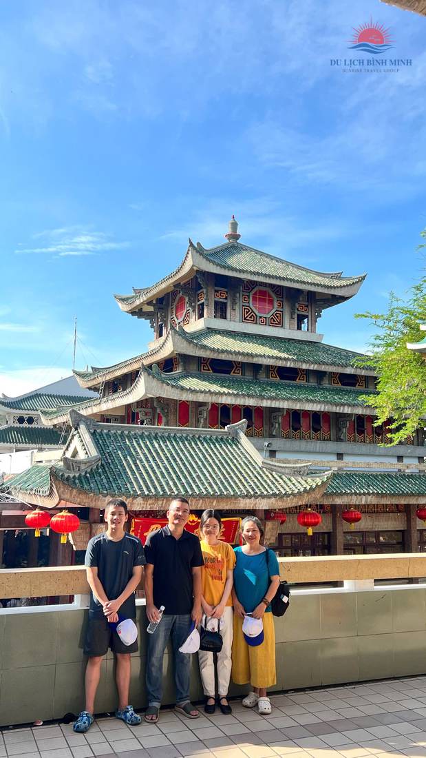 Gia đình du khách check-in với tháp mái cong ngói xanh của Miếu Bà Chúa Xứ núi Sam trên nền trời xanh, lồng đèn đỏ