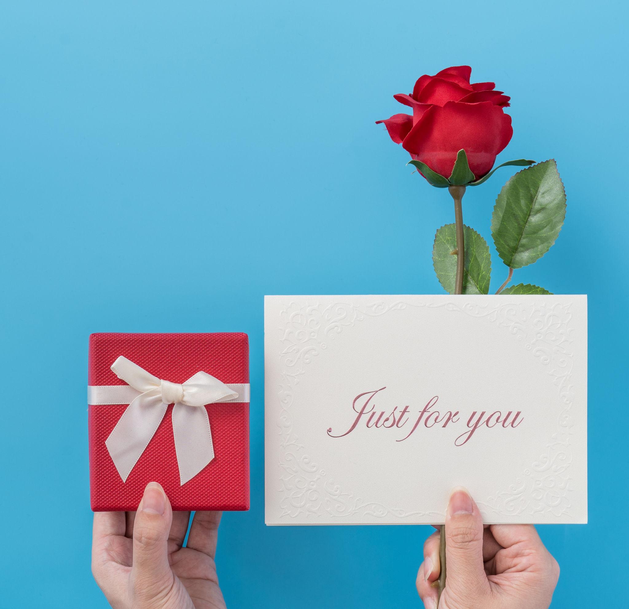 bàn tay cầm hộp quà và thiệp chúc mừng cùng bông hồng đỏ