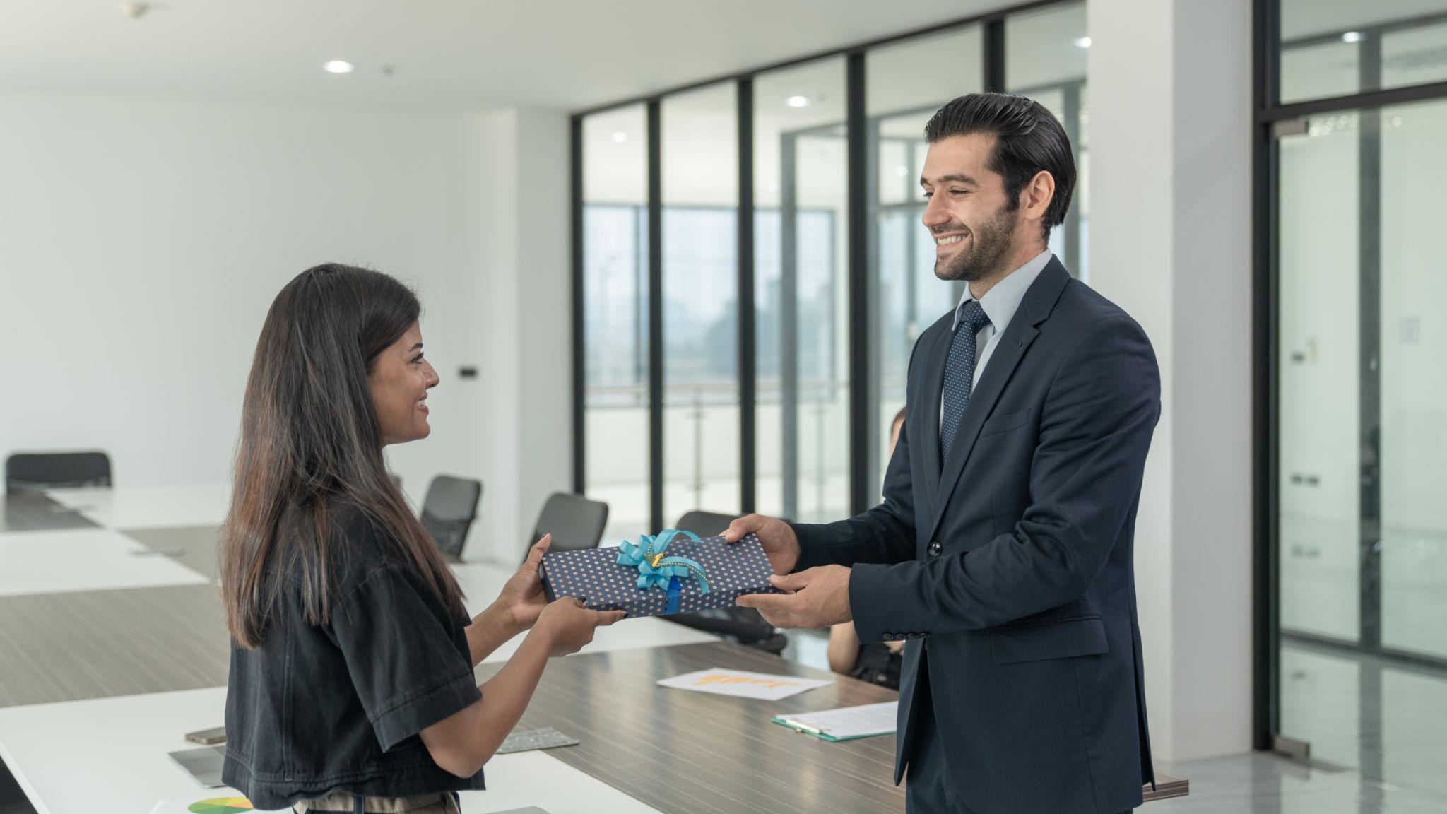 người đàn ông đang trao quà tặng cho người phụ nữ trong văn phòng doanh nghiệp