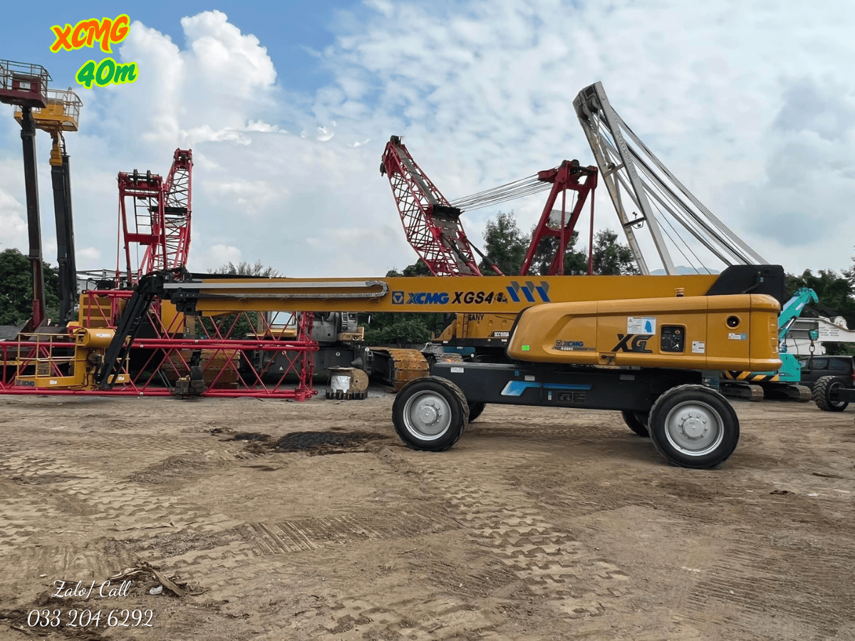 Toàn cảnh xe nâng người boom lift XCMG 40m màu xanh đặc trưng đang làm việc hiệu quả, giúp công nhân tiếp cận mặt ngoài của một công trình lớn