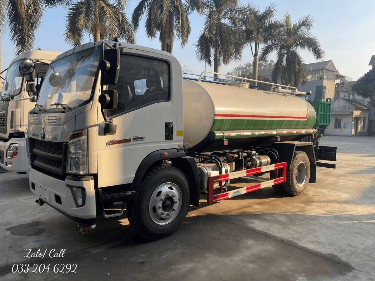Toàn cảnh xe téc Howo phun nước 9 khối màu xanh đặc trưng đang vận hành trên đường phố.