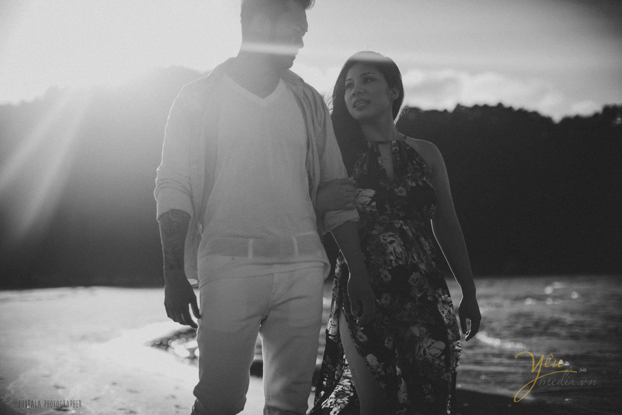 ảnh đen trắng cô dâu chú rể nắm tay nhau đi trên biển ánh nắng chiều chiếu nhẹ