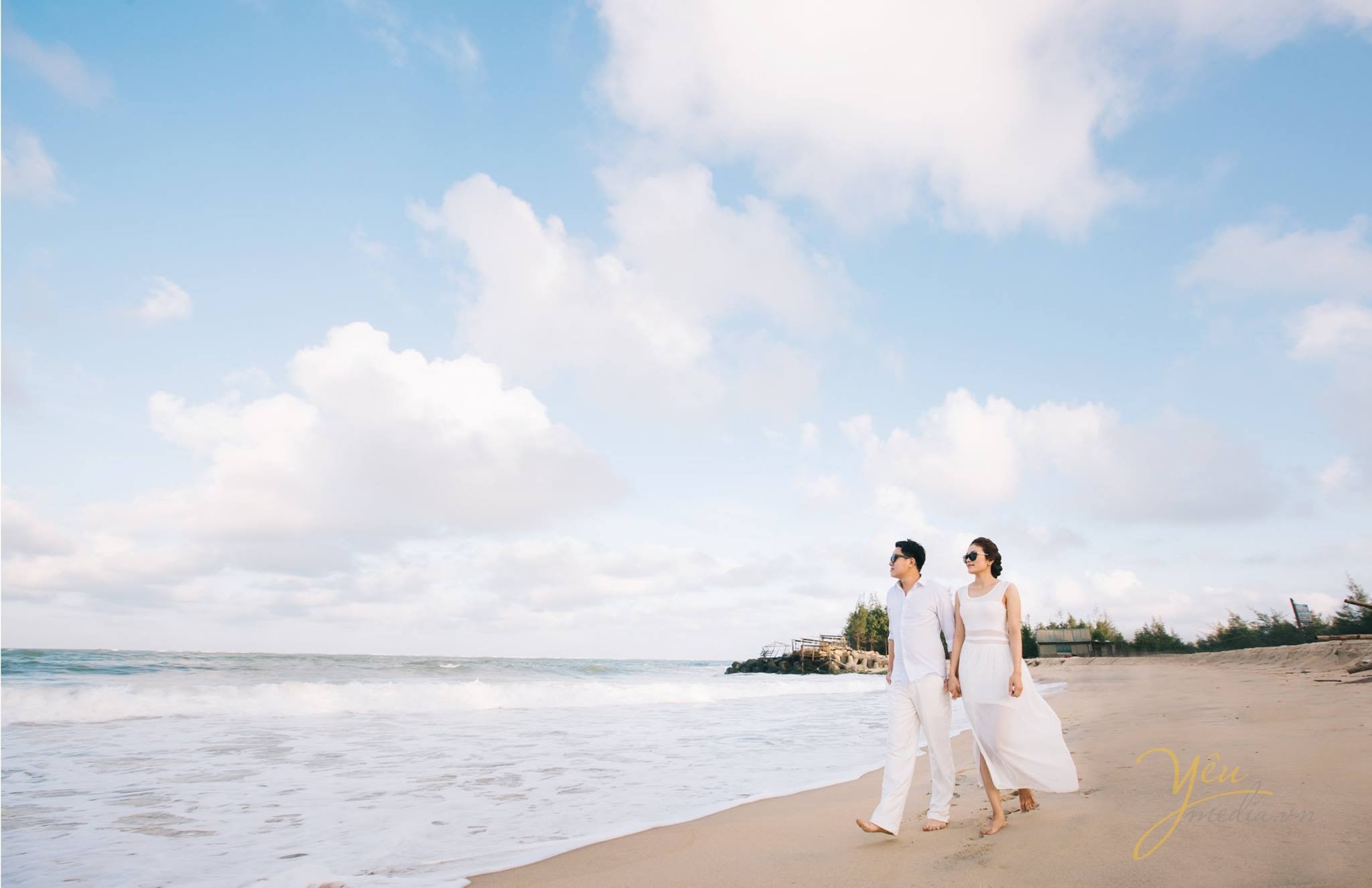 cô dâu chú rể nắm tay đi dạo trên bờ biển