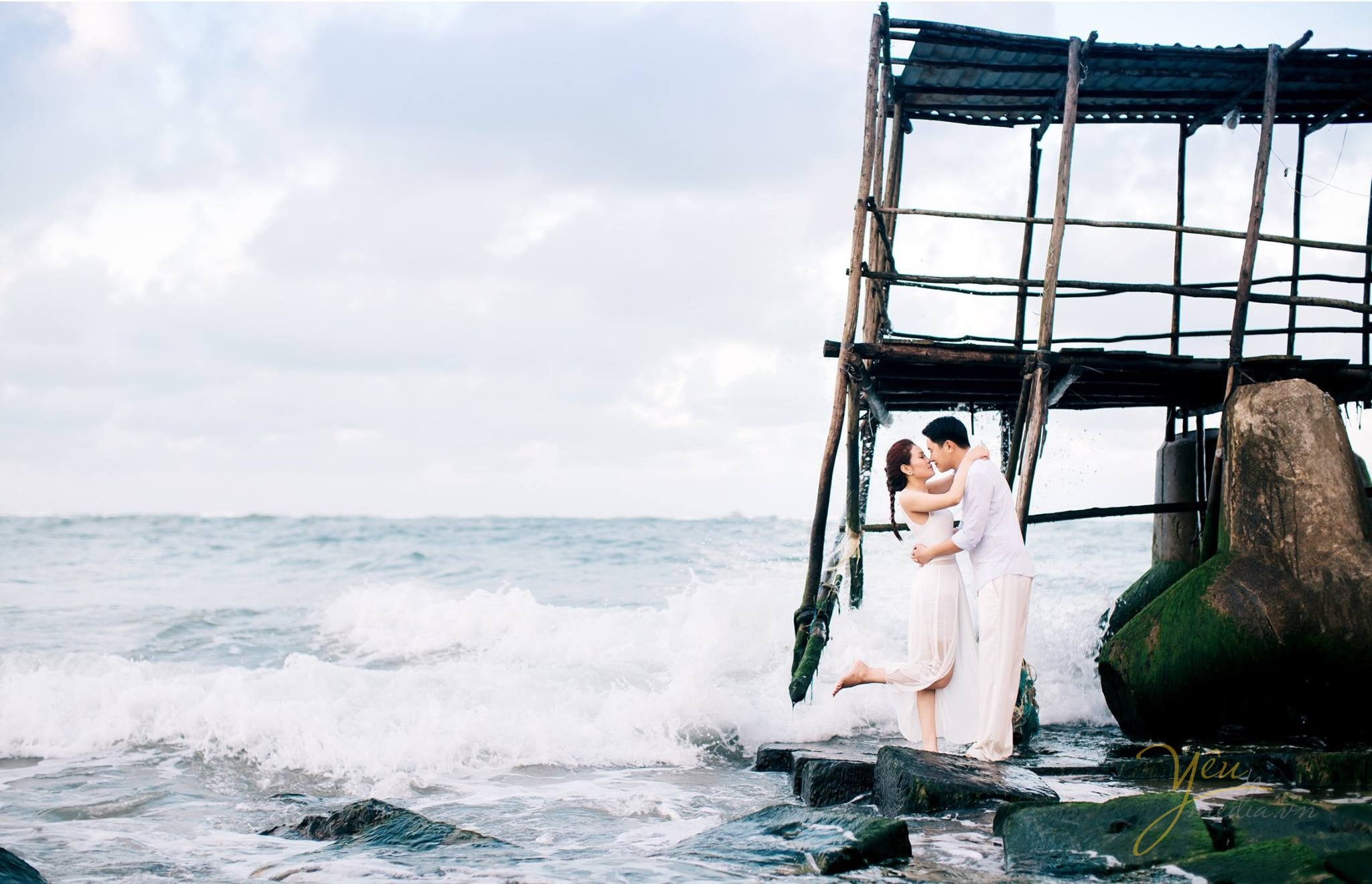 cô dâu chú rể hôn nhau trước chòi canh trên biển