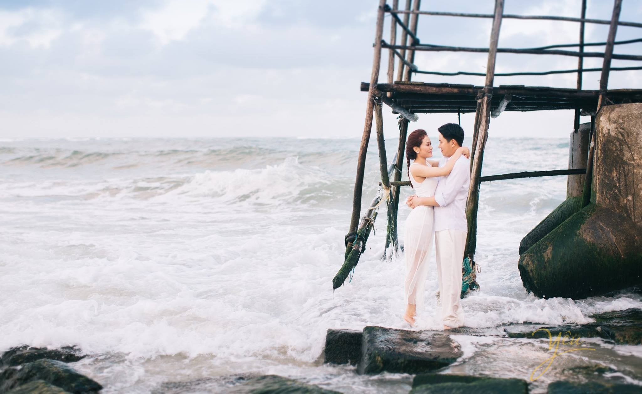 cô dâu chú rể ôm nhau trước chòi canh trên biển