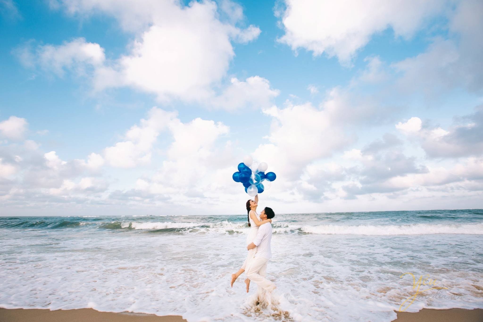chú rể bế cô dâu dưới chân sóng biển đánh bọt trắng xóa