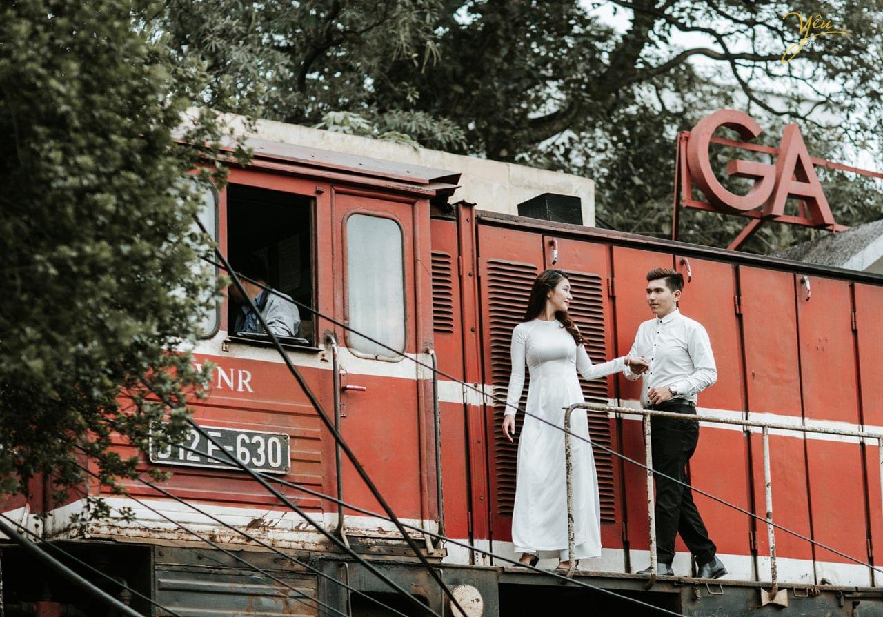 ảnh cưới áo dài trắng chú rể nắm tay cô dâu đi cạnh ga tàu hỏa