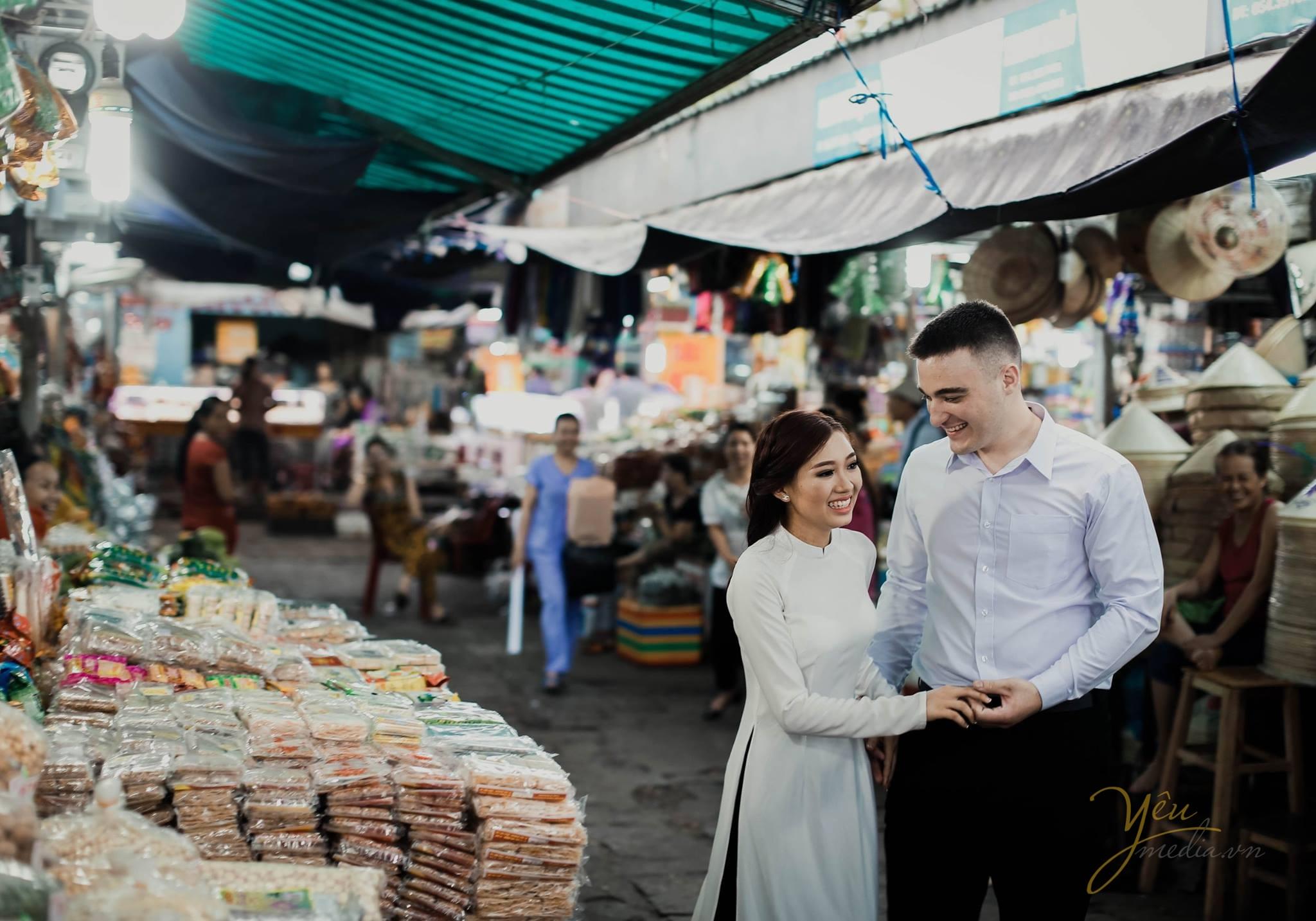 ảnh cưới chụp tại chợ cô dâu chú rể cười nói tự nhiên cạnh hàng bánh kẹo