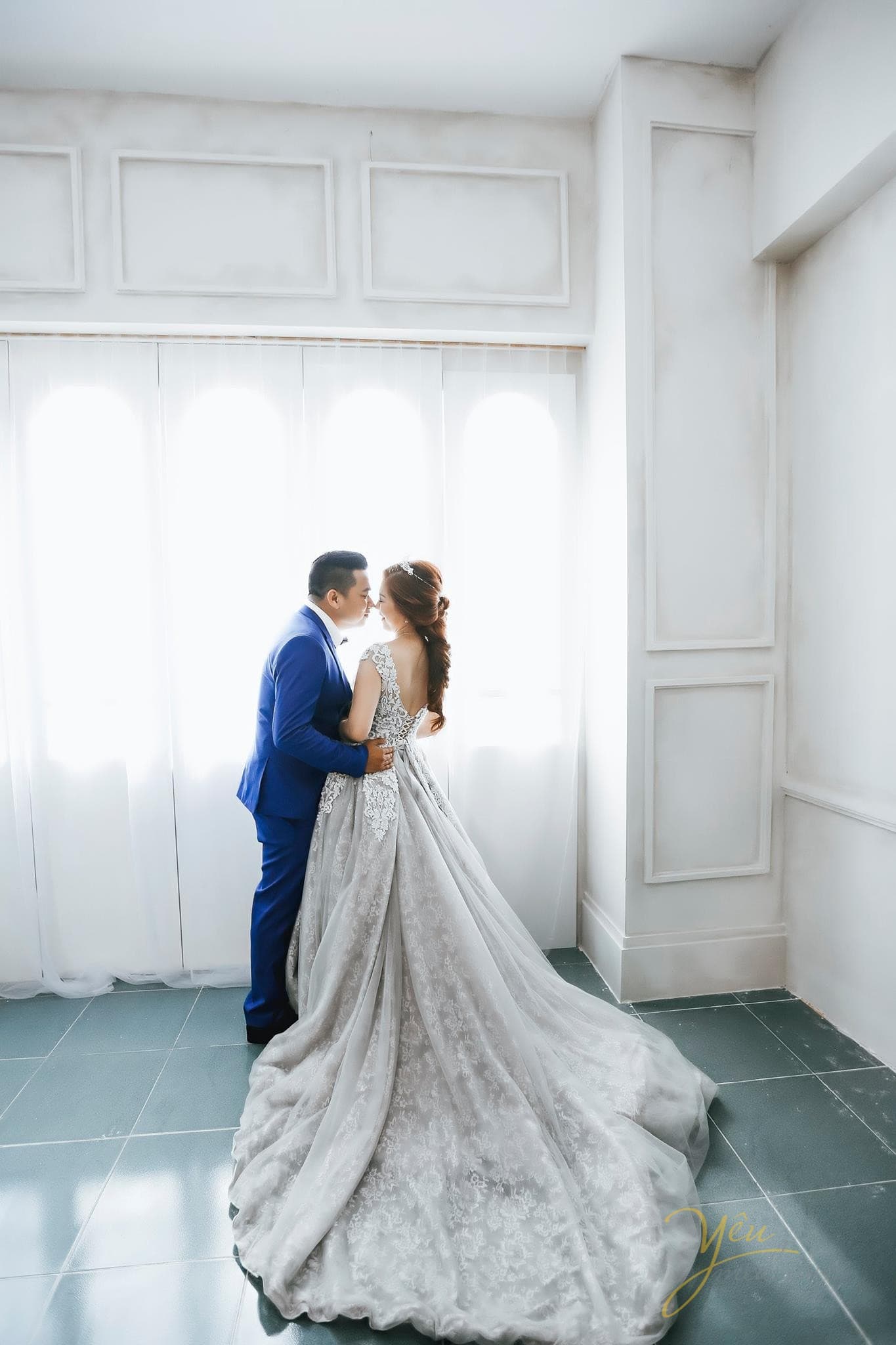 chú rể hôn nhẹ cô dâu trong ánh sáng khung cửa sổ