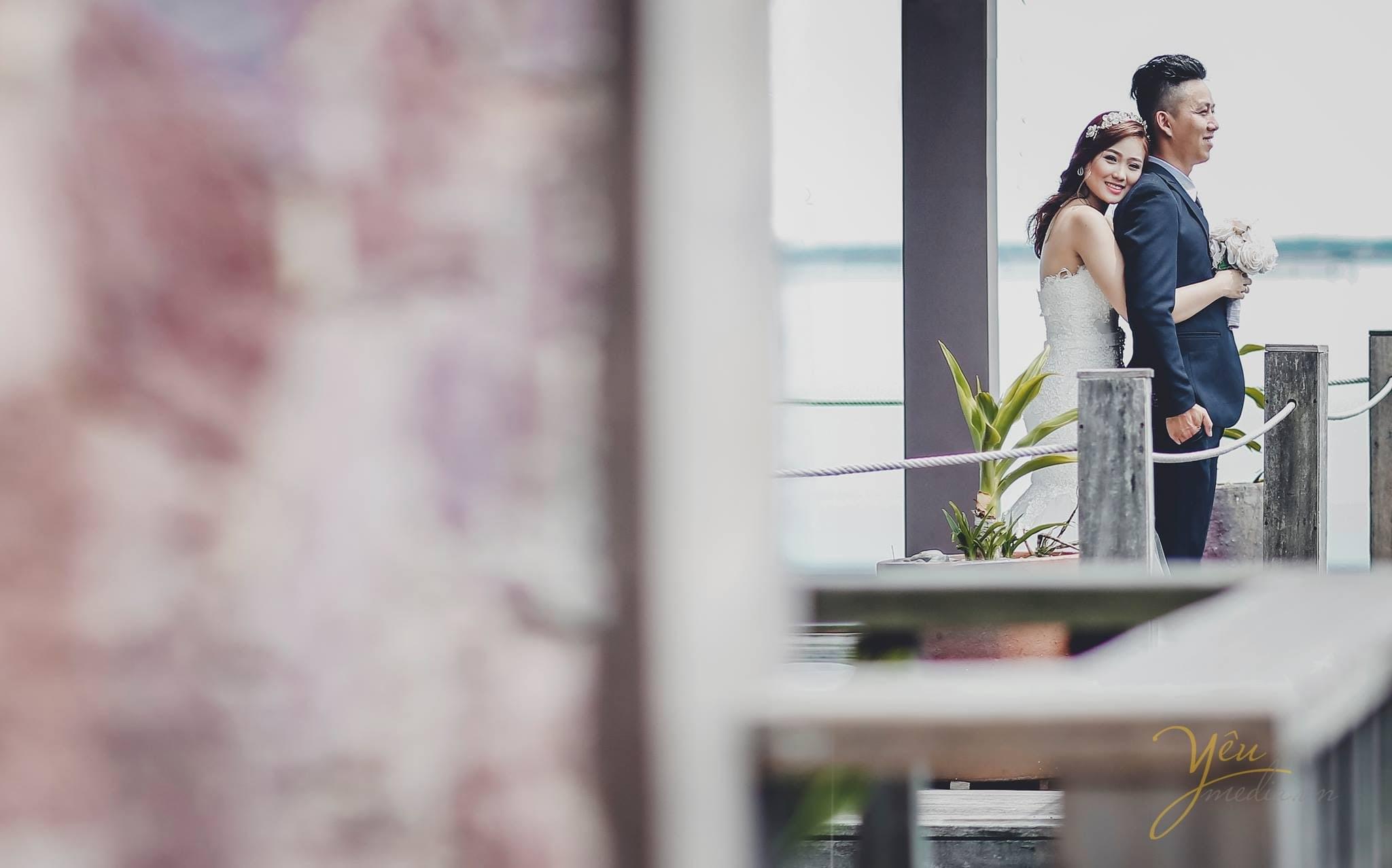 ảnh chụp cô dâu ôm từ phía sau lưng chú rể đứng trên cầu