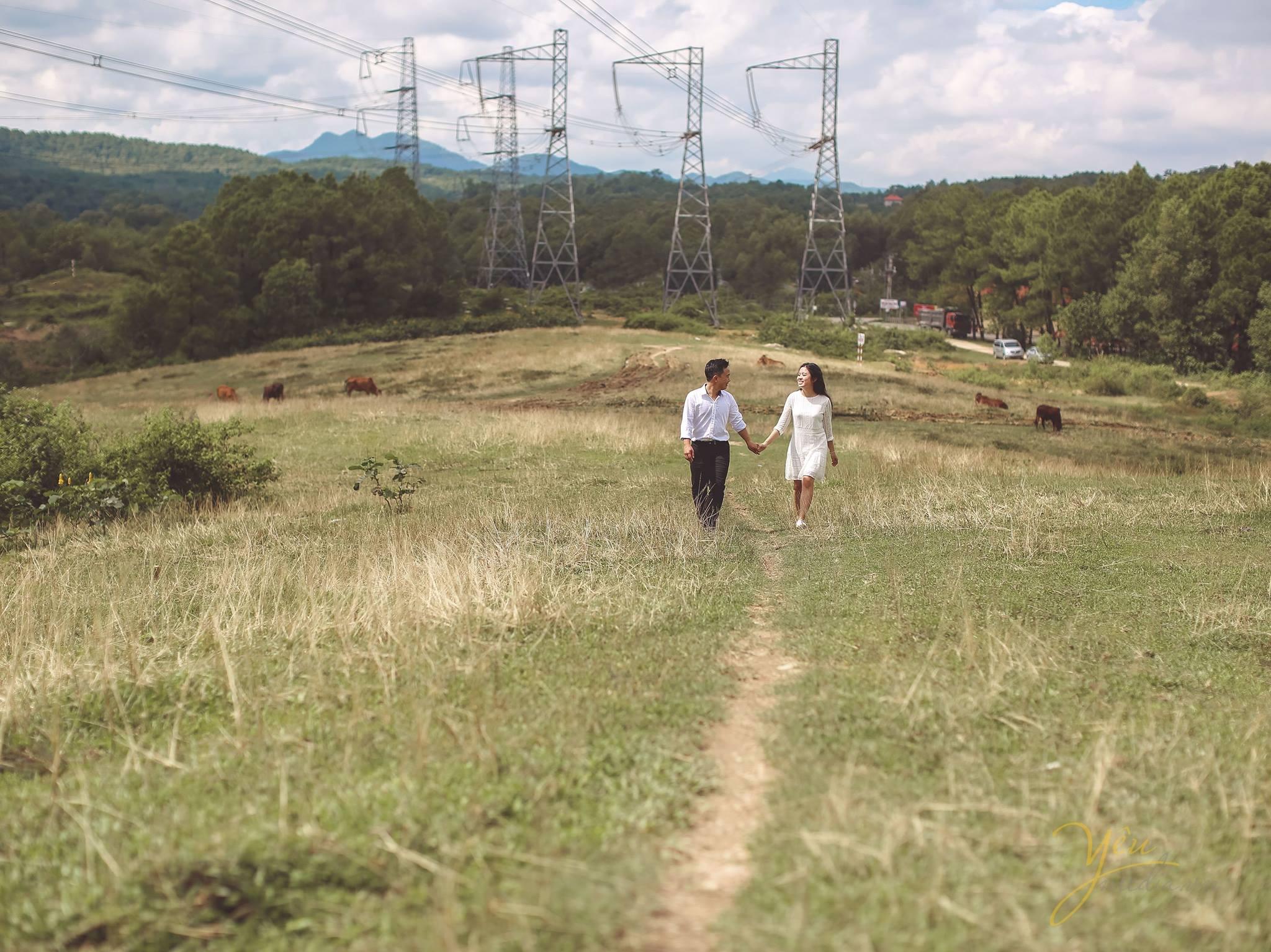 ảnh chụp từ xa cô dâu chú rể nắm tay nhau bước đi phía sau là núi đồi trập trùng
