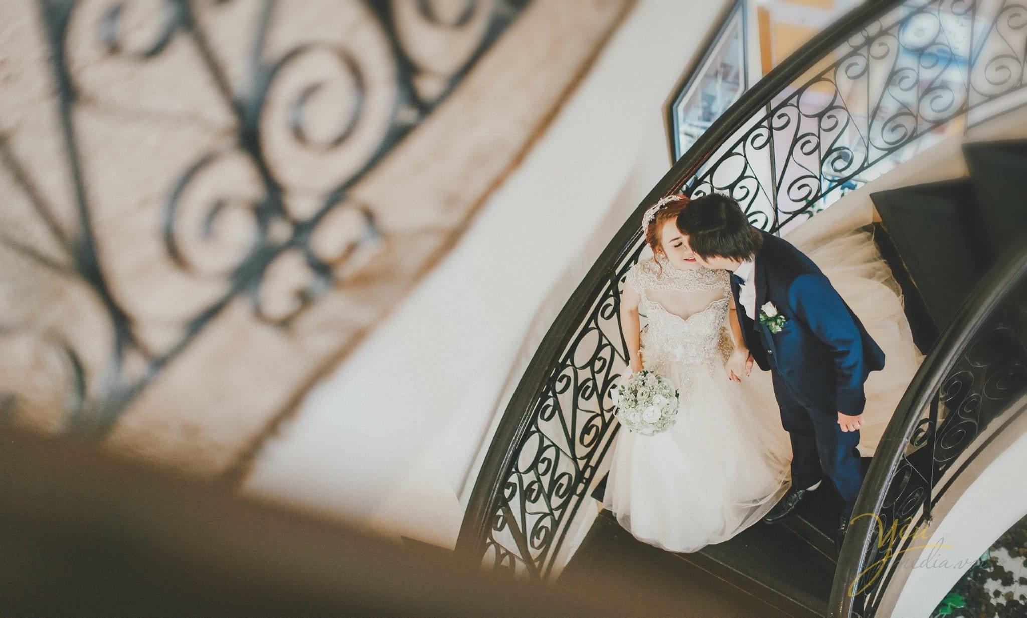 ảnh phóng sự cưới chụp từ xa cô dâu chú rể nắm tay nhau đi xuống cầu thang
