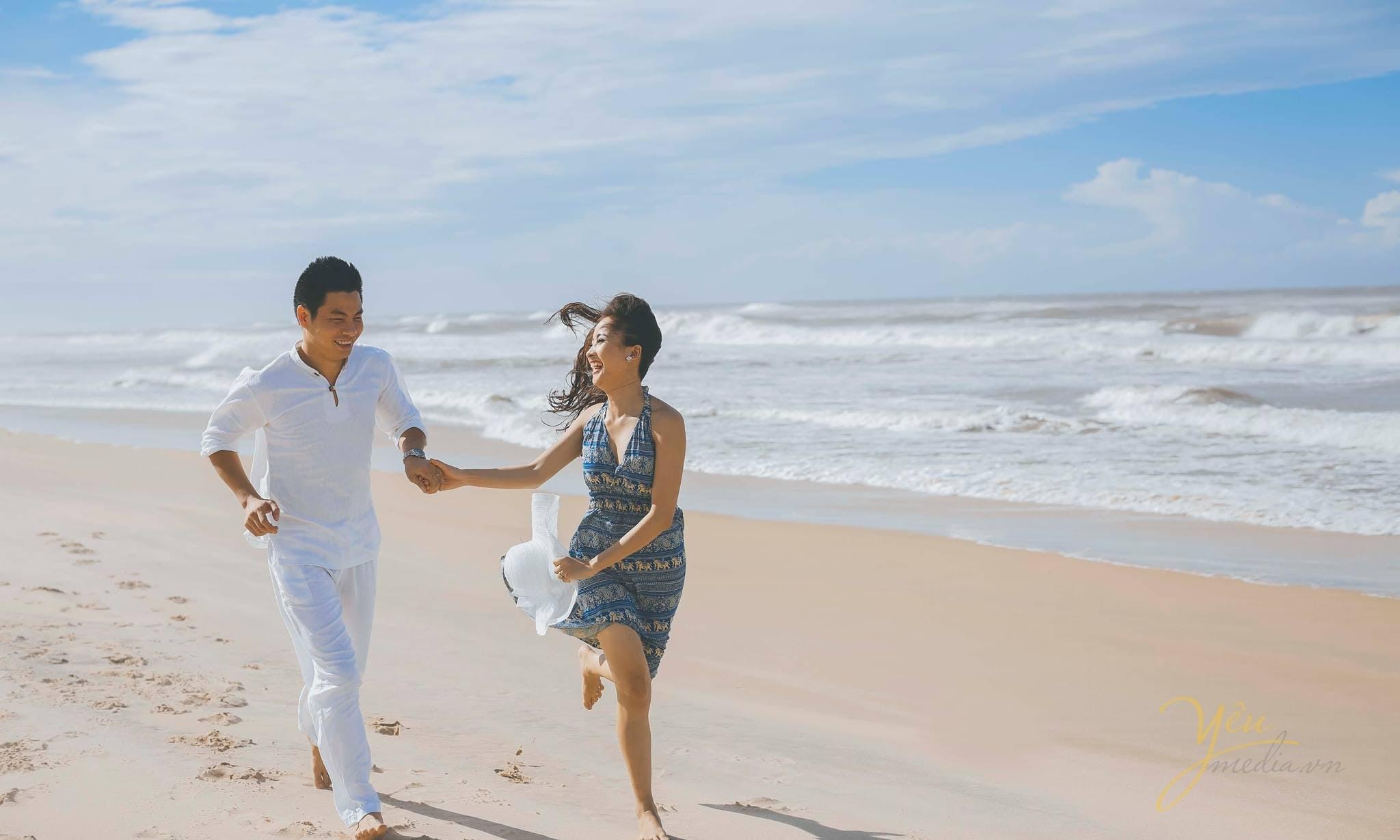 cô dâu chú rể nắm tay chạy trên cát bờ biển