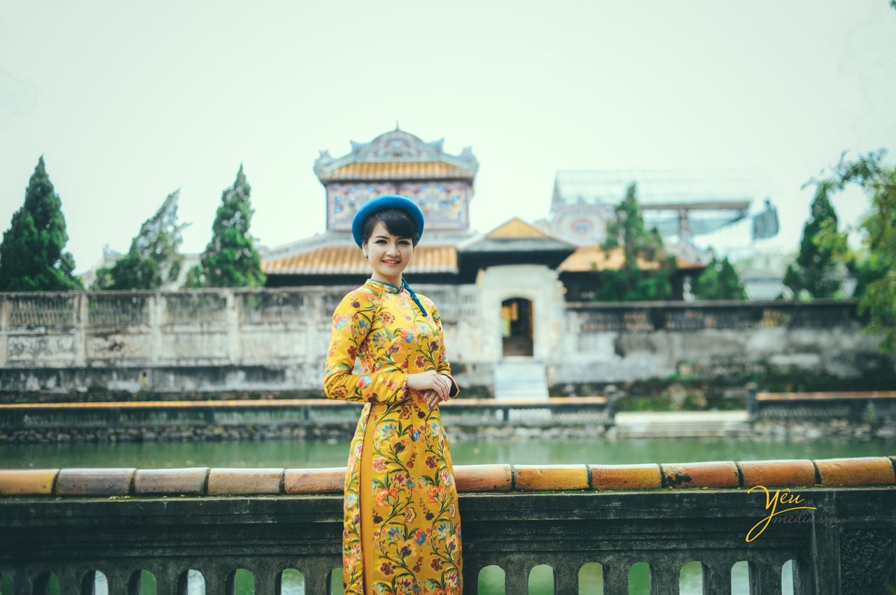 ảnh cưới cô dâu mặc áo dài gấm màu vàng đứng bên hồ