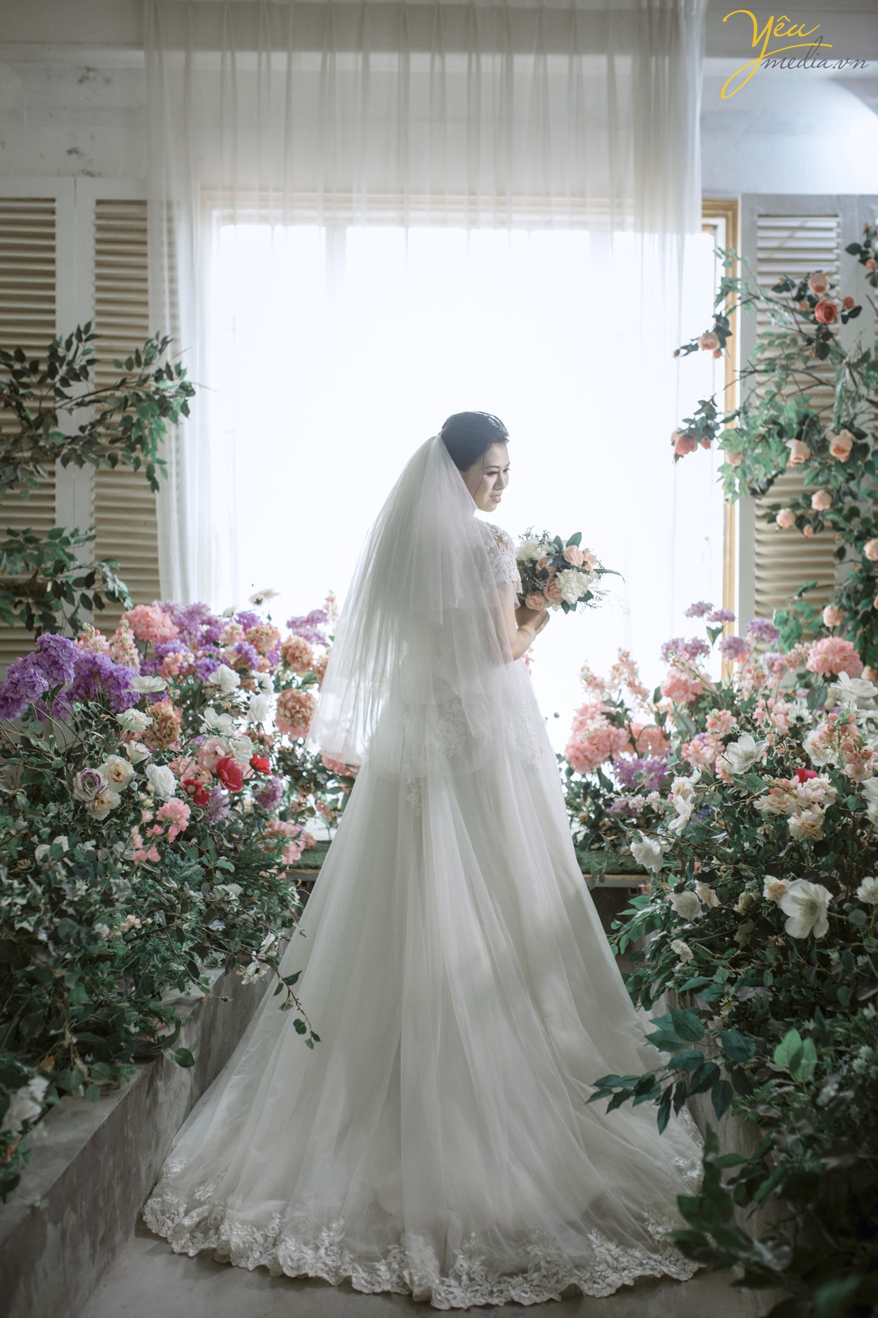 cô dâu đứng quay lưng chụp ảnh trong vườn hoa phim trường