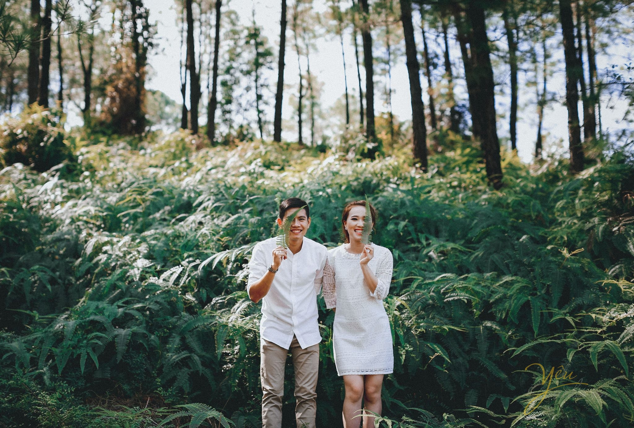 ảnh cưới ngoại cảnh chụp cô dâu chú rể dùng lá cây che mặt