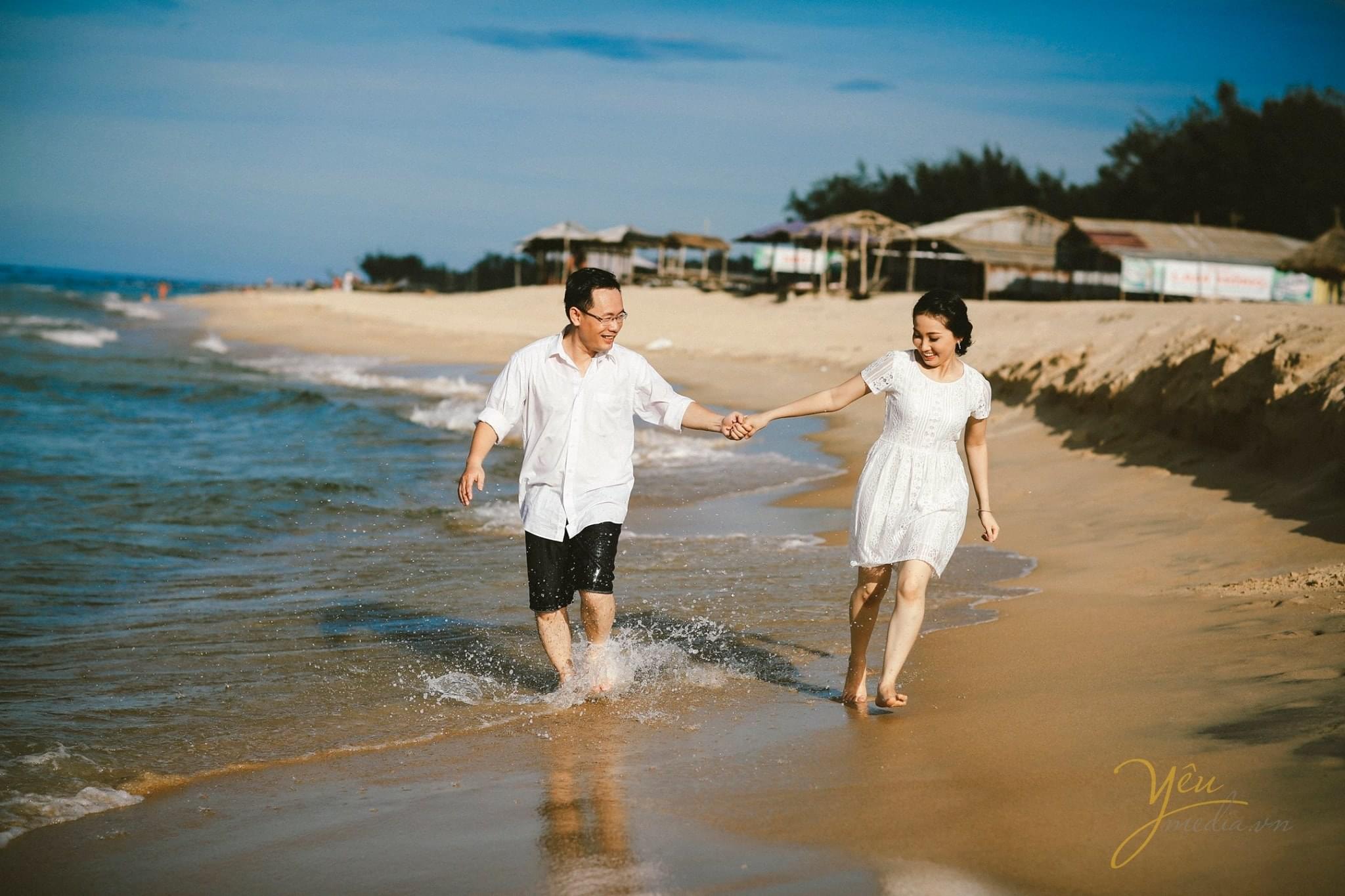 cô dâu chú rể nắm tay nhau chạy trên biển