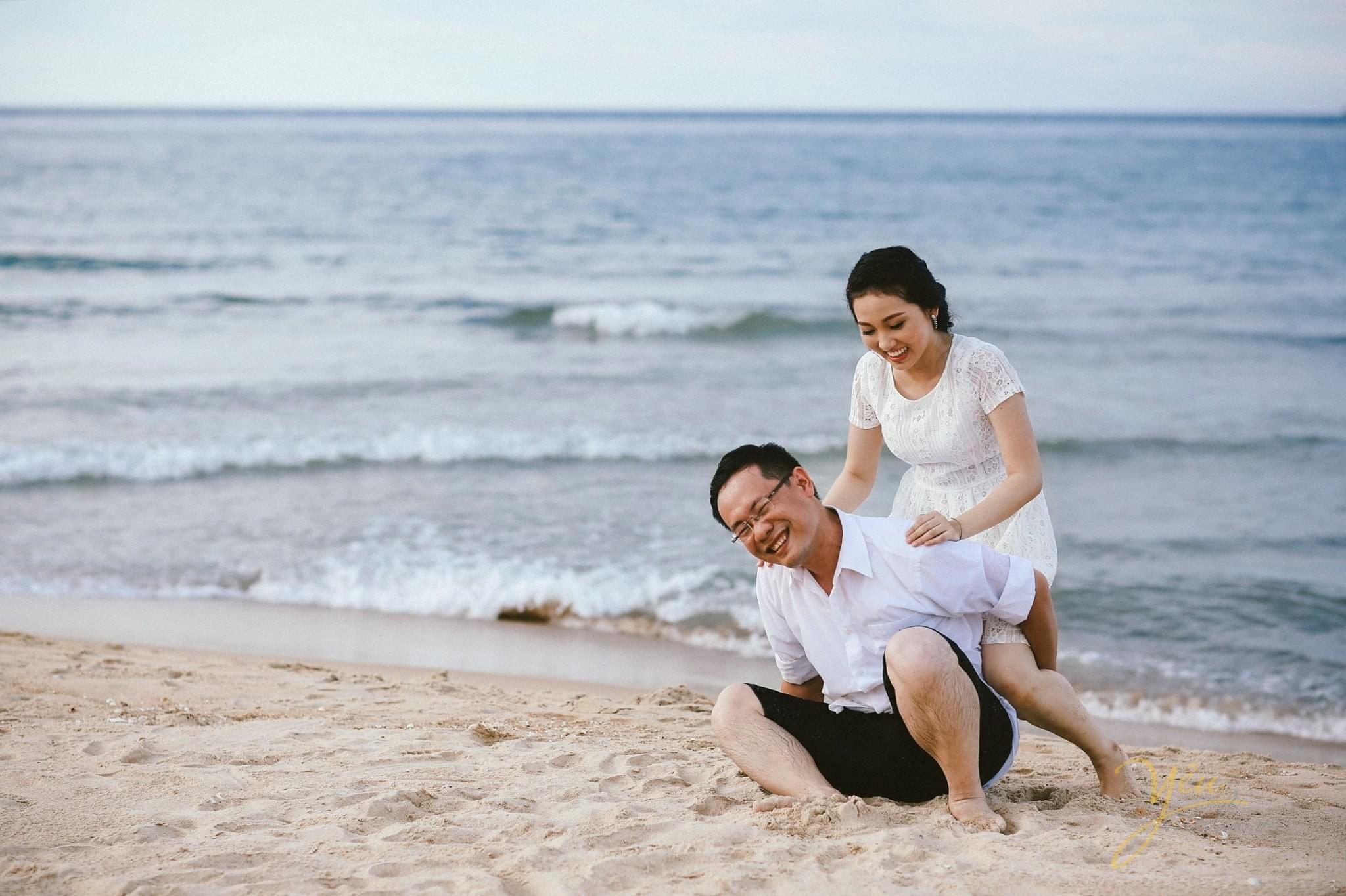 chú rể ngồi xuống cõng cô dâu trên biển