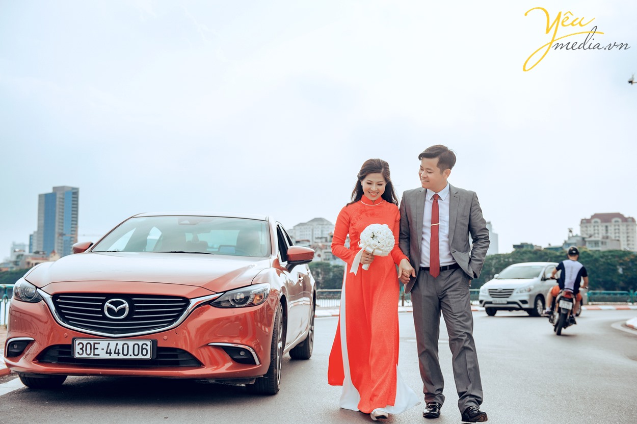 cô dâu dài áo đỏ chụp cùng chú rể bên xe hơi