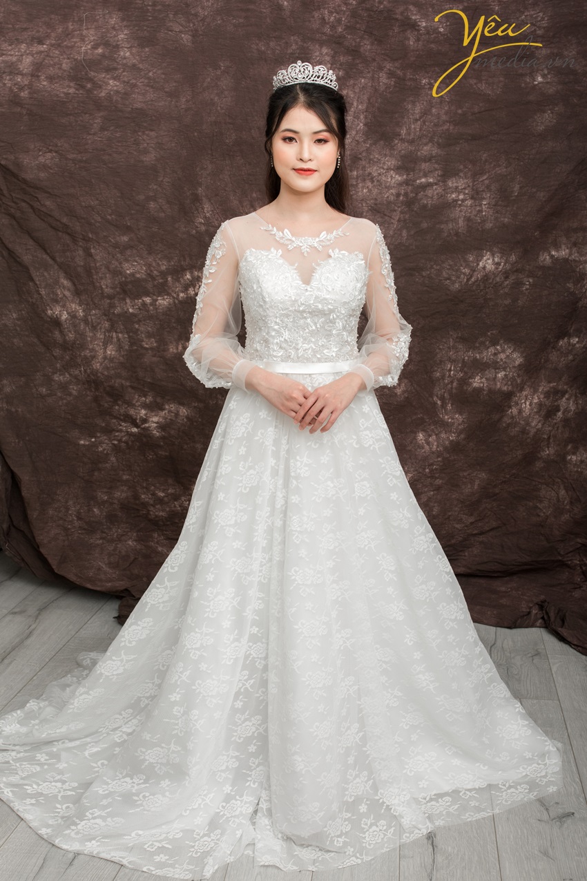 Một chiếc váy nhẹ nhàng và đáng yêu dành cho những cô dâu thích vẻ ngoài hiền thục và nhu mì trong ngày cưới của mình.   Với phần ren nhẹ nhàng, tay dài hơi bồng thoải mái, cúp ngực kín đáo, đai eo sang trọng và phần vải ren thân váy hoa chìm đẳng cấp - đây là chiếc váy đã khiến nhiều cô dâu "Say yes to the dress" của Yêu Media.