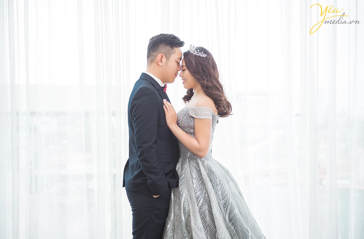 cô dâu chú rể chụp ảnh bên khung cửa sổ đầy ánh sáng