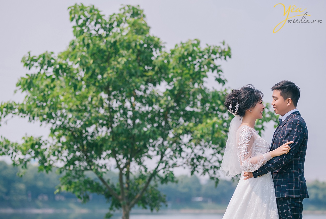 ảnh cưới cô dâu chú rể đứng trước hàng cây xanh