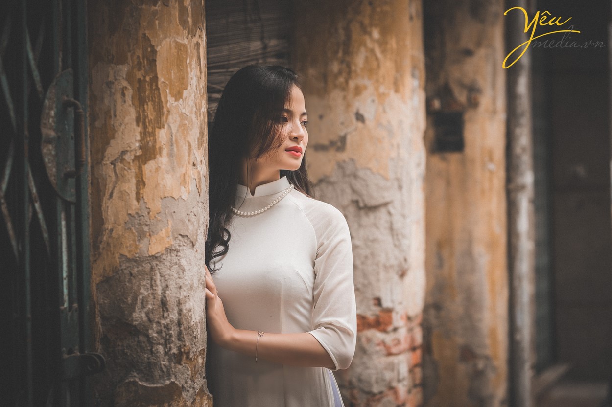 cô gái hà nội mặc áo dài màu trắng đứng nép tường