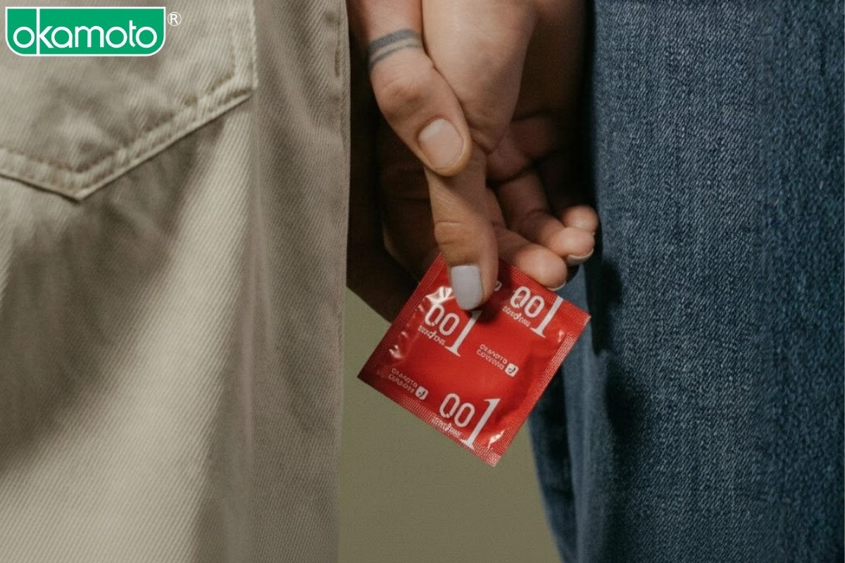 Bàn tay của một cặp đôi cùng nhau cầm bao cao su OKAMOTO 0.01