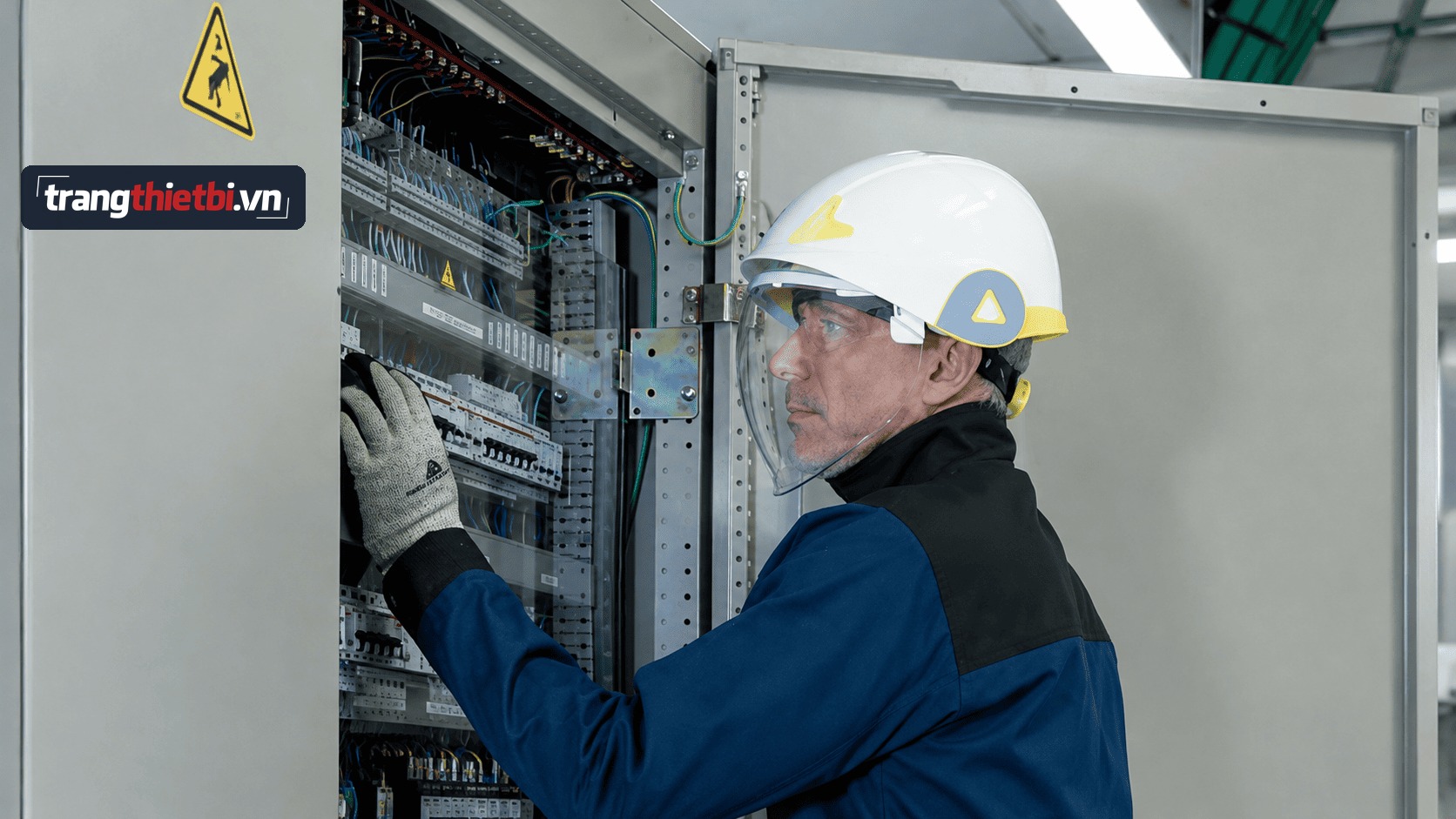 Kỹ thuật viên điện đội mũ bảo hộ gắn kính che mặt chống hồ quang đang thao tác kiểm tra bảo trì tủ điện công nghiệp