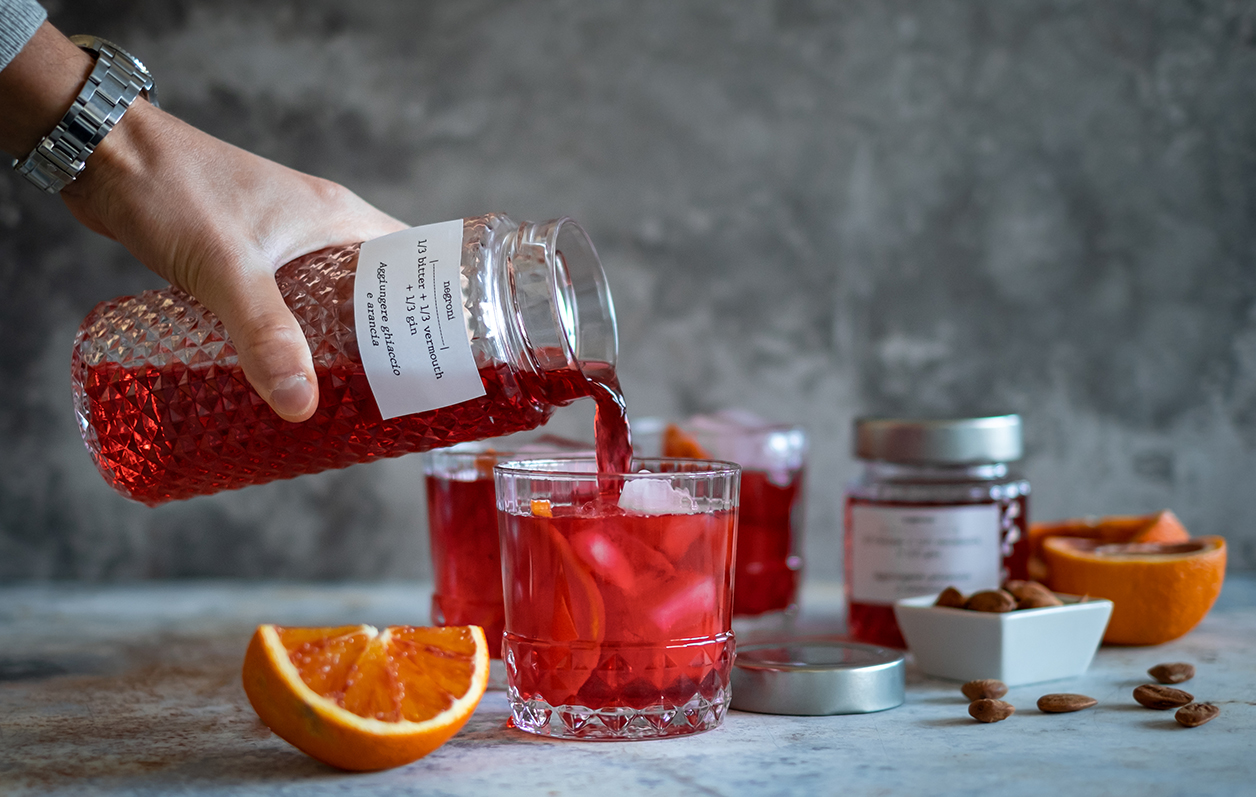 tay rót đồ uống màu đỏ từ hũ thủy tinh họa tiết nổi vào ly có đá và cam