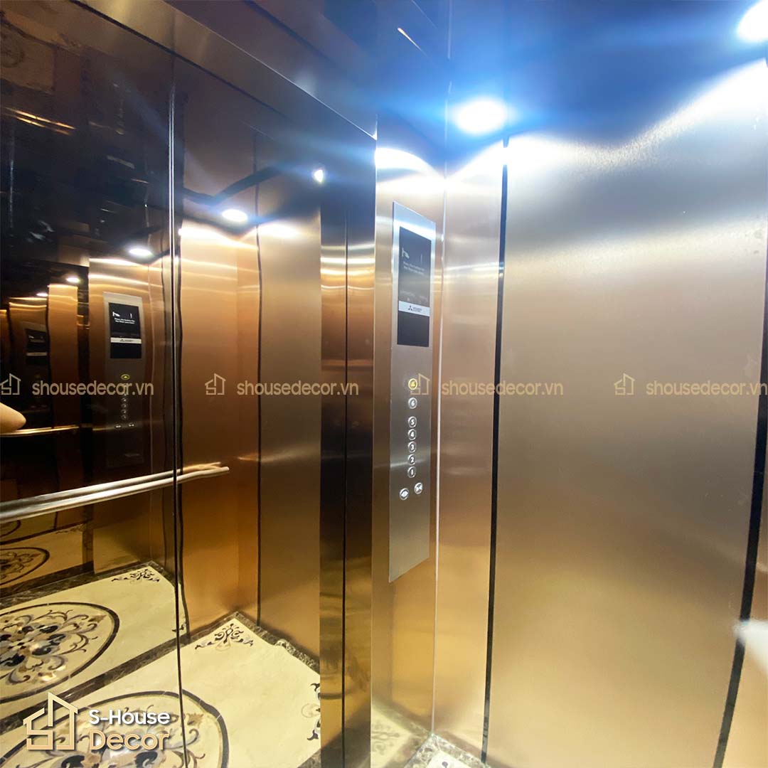 Cabin thang máy cao cấp với nội thất trắng gương, laminate giả kim màu đồng và xám – phối màu hài hòa, hiện đại.