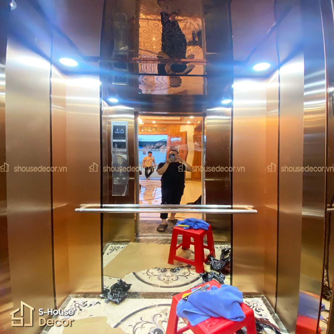 Cabin thang máy phong cách hiện đại, phối màu đồng – xám tinh tế, kết hợp ánh sáng dịu nhẹ từ trần gương trà