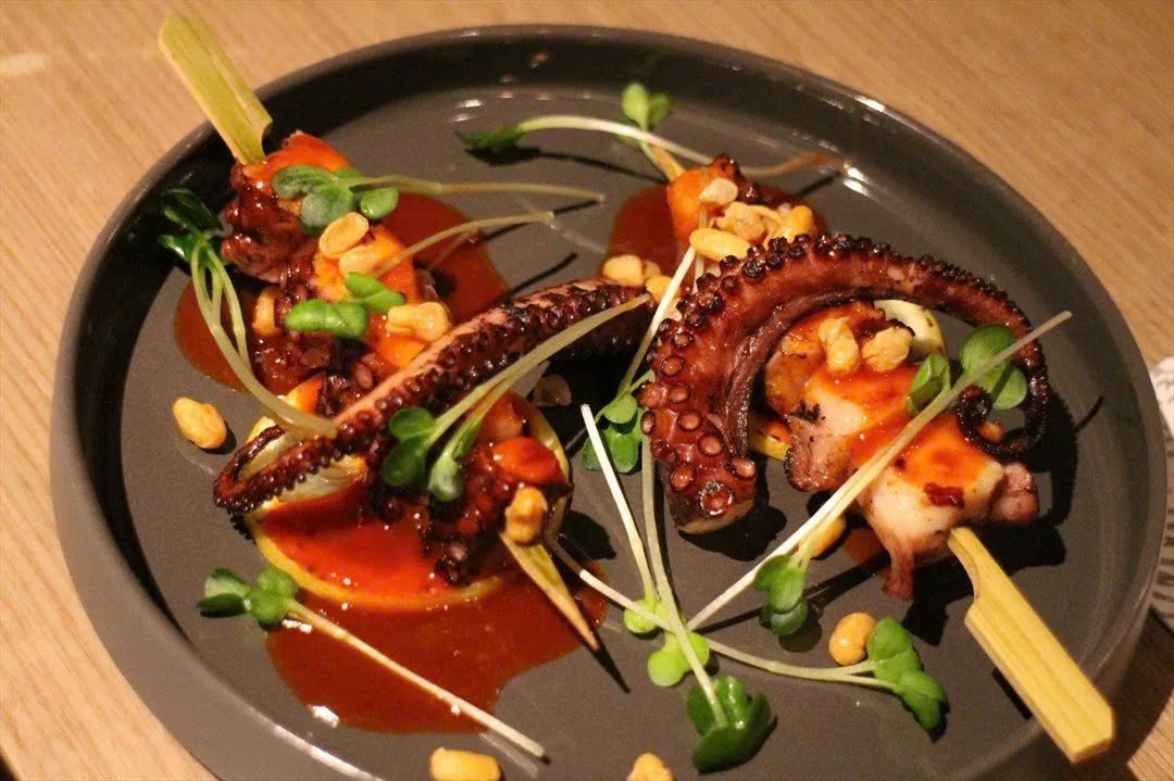 Bạch tuộc khổng lồ nướng sa tế đỏ au trên bếp than, thơm lừng, thịt săn chắc và cháy cạnh hấp dẫn