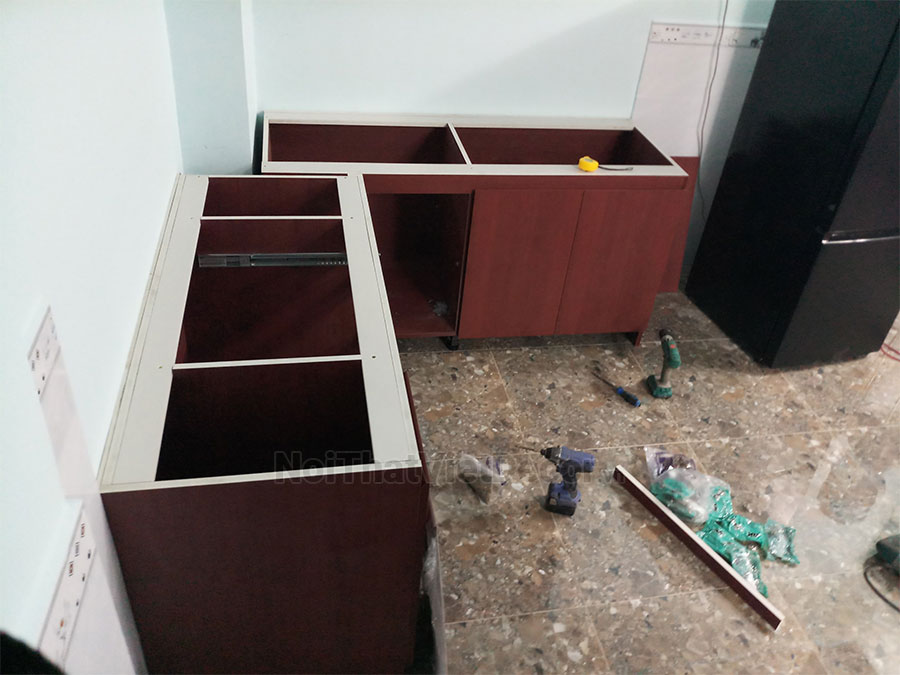 Tủ bếp hiện đại chữ L có vách che, gỗ công nghiệp nhựa WPB An Cường phủ laminate, mặt đá tự nhiên kim sa đen, ốp tường kính cường lực 8mm sơn màu - Hình thi công
