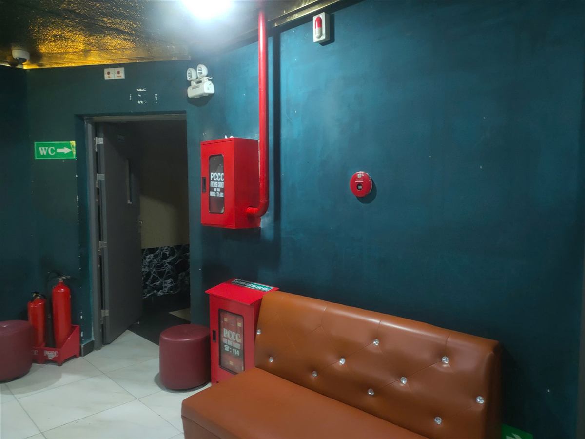 Hành lang có tủ chữa cháy, bình chữa cháy và chuông báo cháy tại cơ sở karaoke