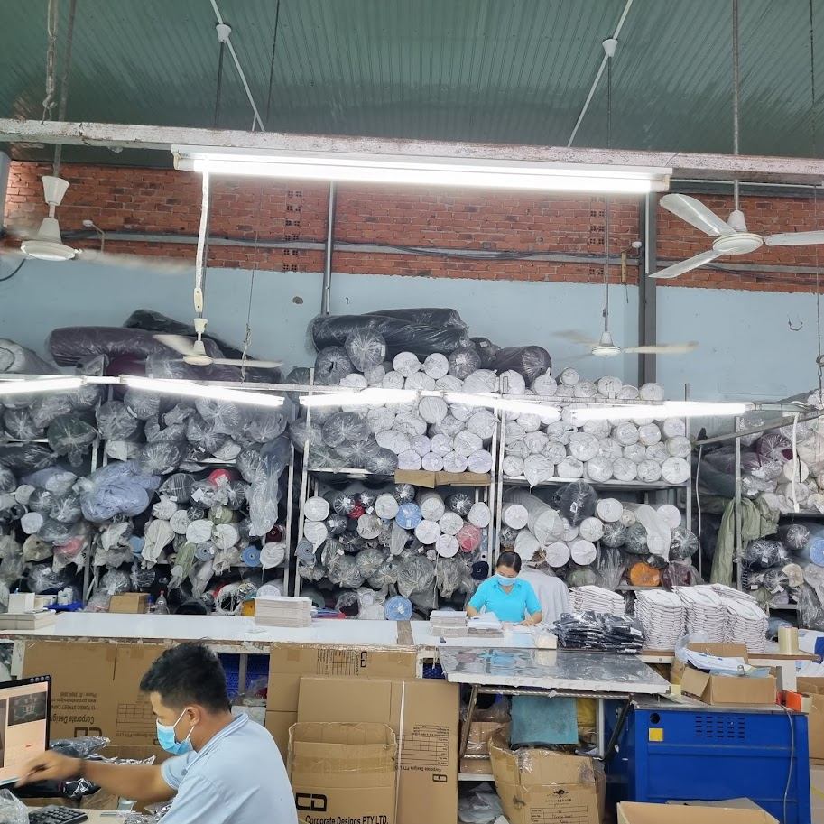 Vải cuộn xếp trên giá cạnh bàn làm việc trong xưởng may