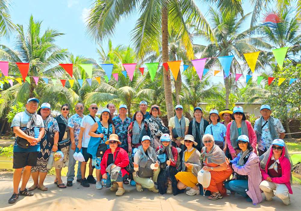 Đoàn khách Du Lịch Bình Minh đội mũ, quàng khăn rằn chụp ảnh tập thể dưới vườn dừa cù lao Thới Sơn, Tiền Giang