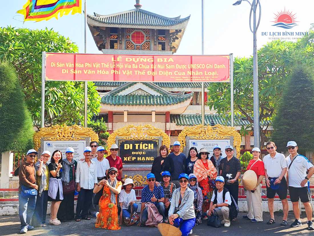 Đoàn khách chụp ảnh trước Miếu Bà Chúa Xứ núi Sam bên băng rôn UNESCO ghi danh Lễ hội Vía Bà và bia Di tích được xếp hạng