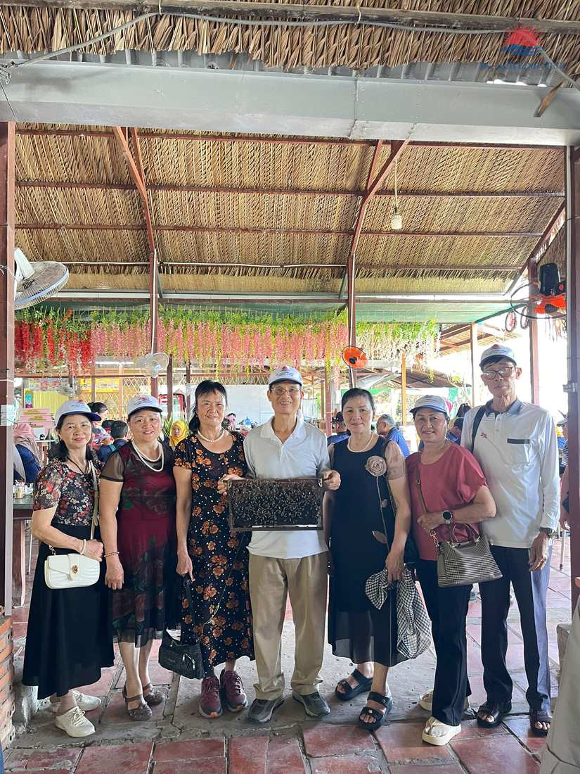 Du khách cầm khung cầu ong phủ kín ong mật khi tham quan trại nuôi ong tại cù lao Thới Sơn, Tiền Giang