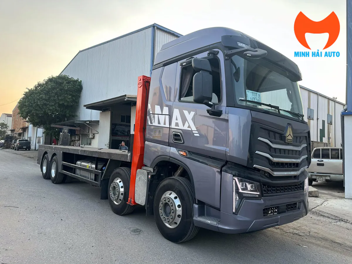 Xe Howo Max màu xám với cabin và sàn chở máy nhìn từ phía trước bên phải