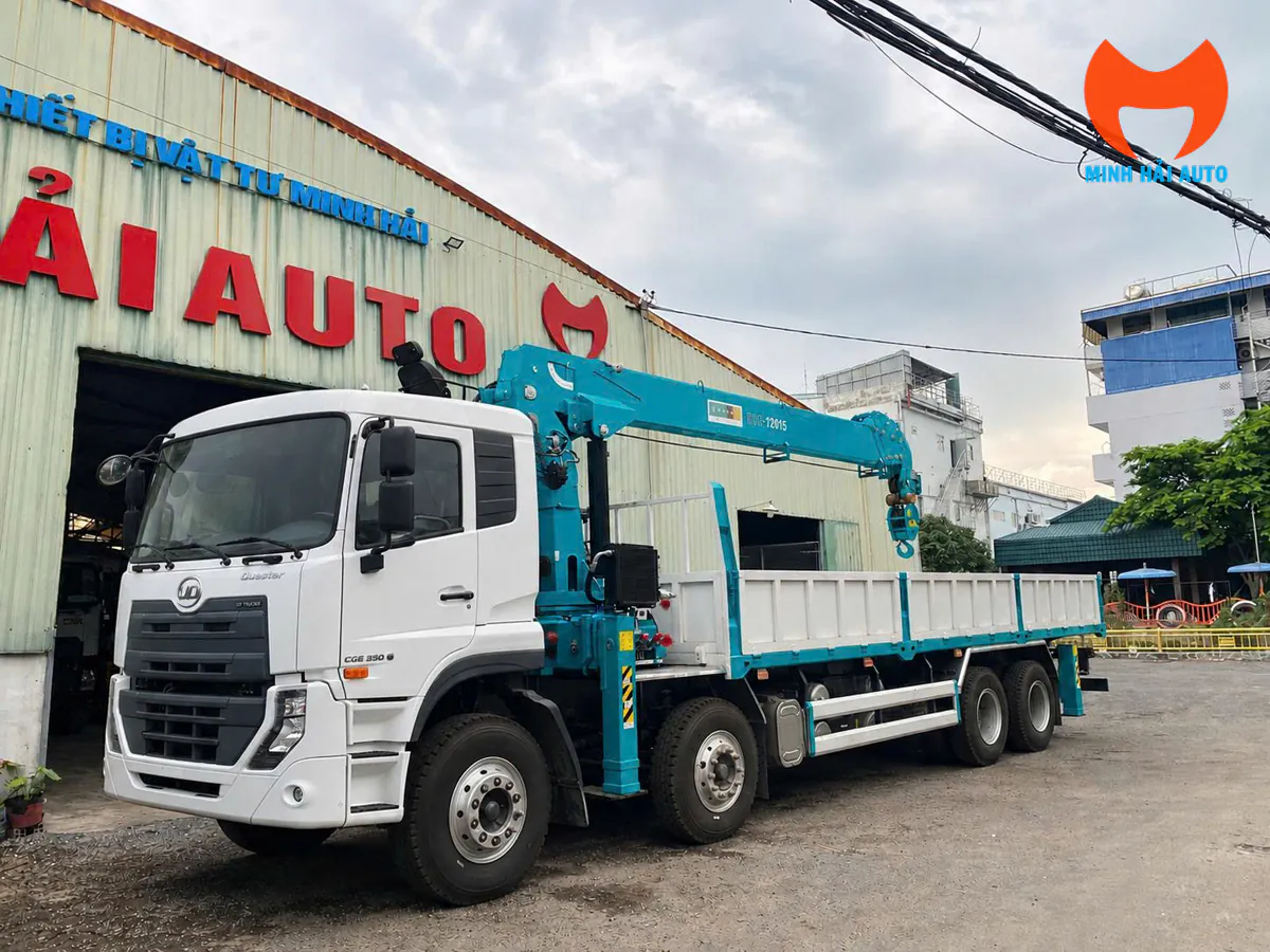 Xe tải bốn chân màu trắng gắn cẩu ống lồng màu xanh ngọc và thùng bửng lật trước dãy nhà xưởng Minh Hải Auto