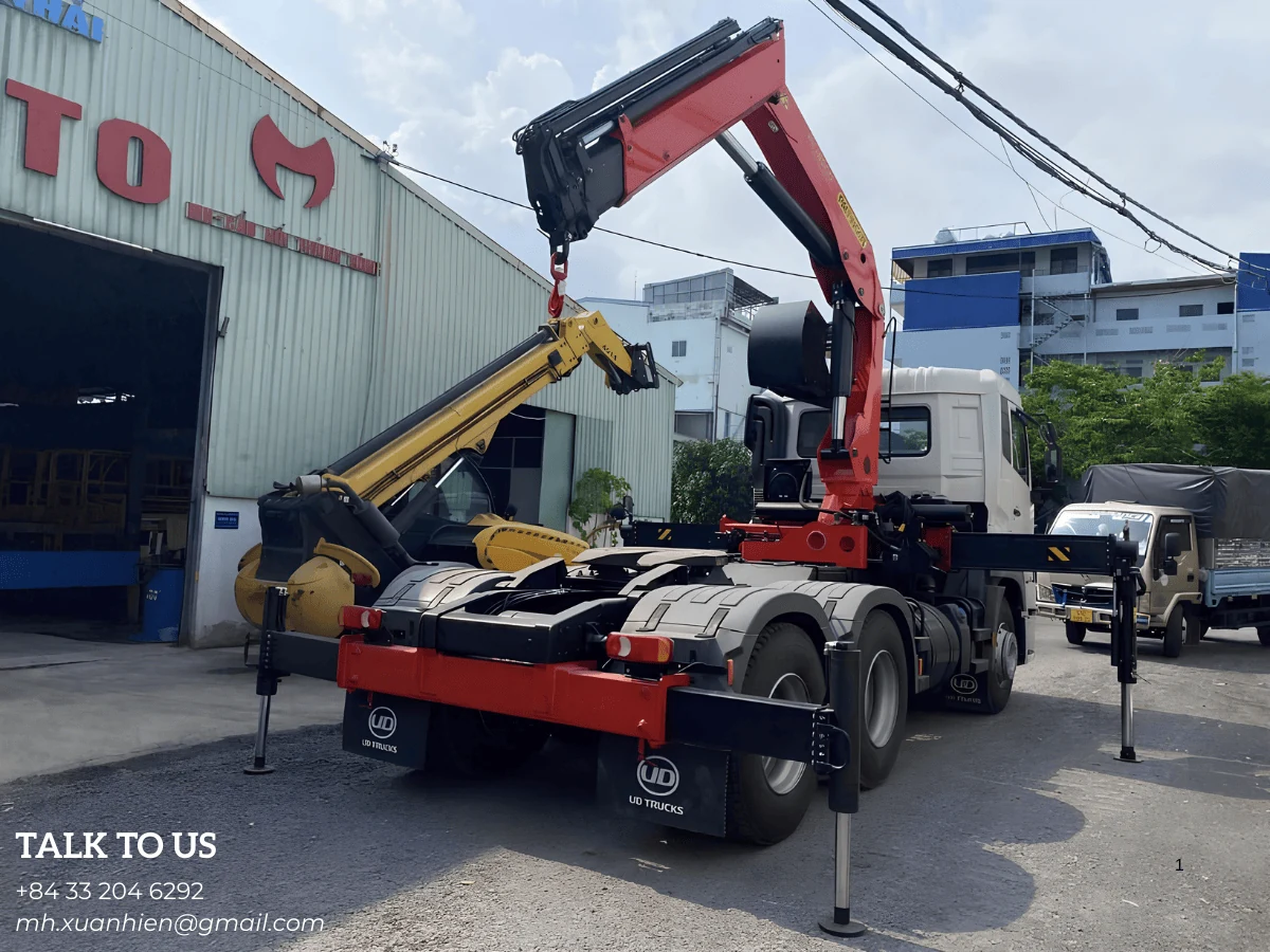 Đầu kéo UD nhìn từ phía sau với cần cẩu Palfinger vươn lên và bốn chân chống hạ xuống nền bê tông trong sân xưởng