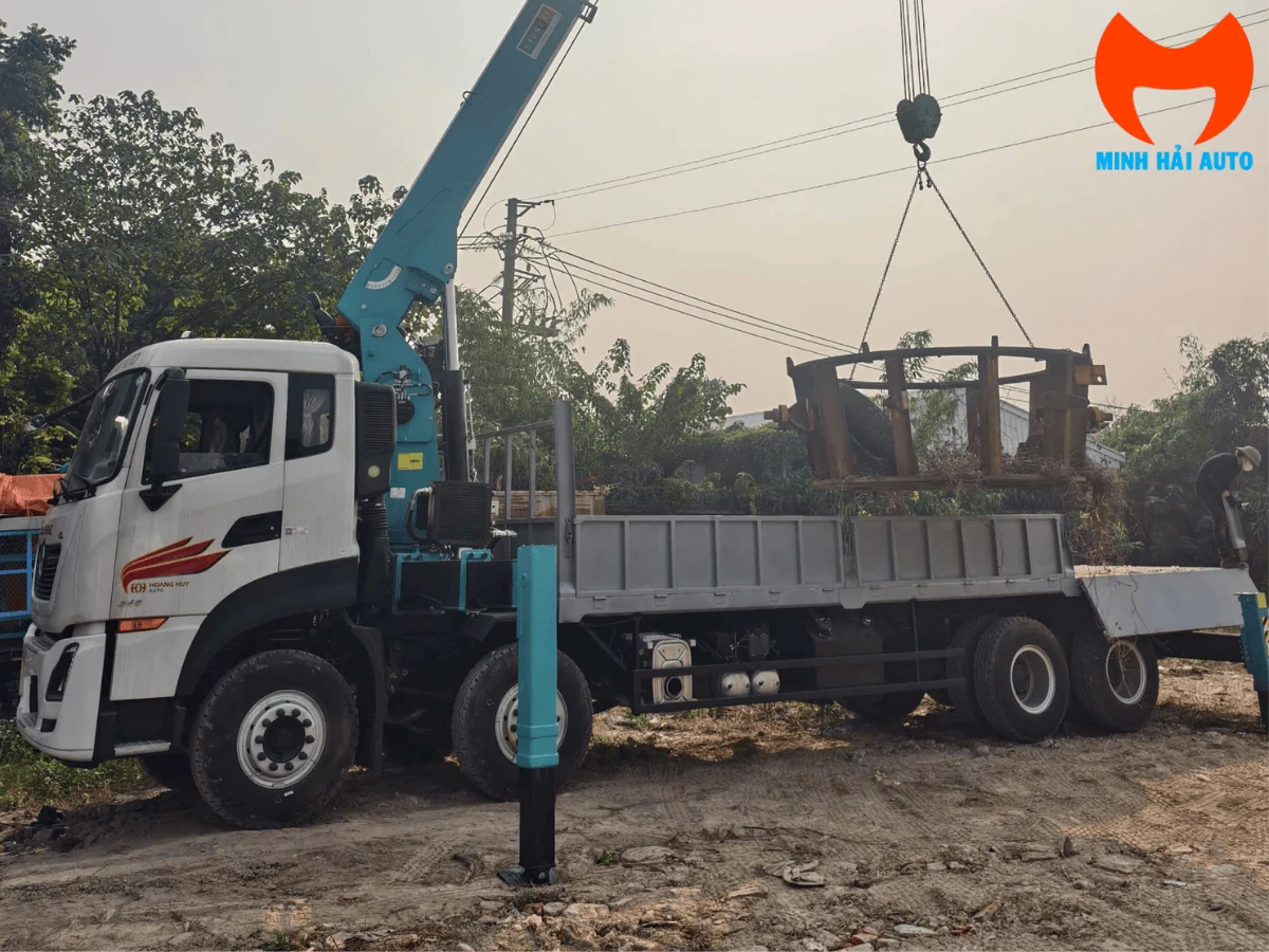 Xe cẩu Dongfeng Hoàng Huy bốn trục đang dùng cẩu nâng lồng thép tại công trường nền đất, chân chống hạ xuống