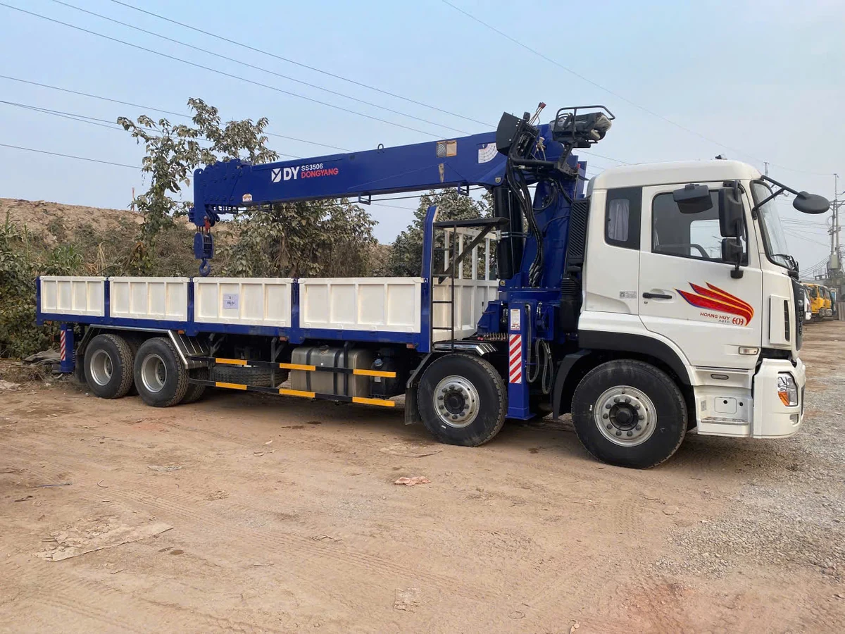 Xe cẩu Dongyang SS3506 nhìn ngang, cần cẩu thu gọn nằm dọc phía trên thùng lửng, chân chống thu vào sát thân xe