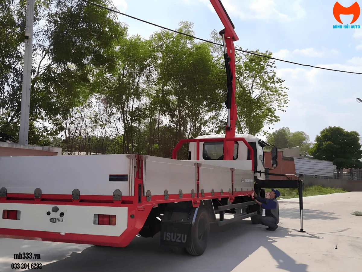 Xe tải Isuzu FRR 650 thùng lửng trắng đỏ với chân chống cẩu hạ xuống nền bê tông, một kỹ thuật viên đang kiểm tra phía bên hông xe
