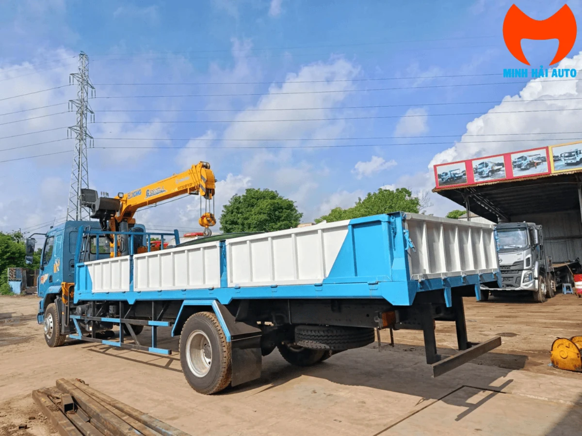 Xe tải Chenglong M3 cabin xanh dương nhìn từ phía sau bên trái, thùng lửng dài và cần cẩu XCMG xếp gọn phía trước thùng