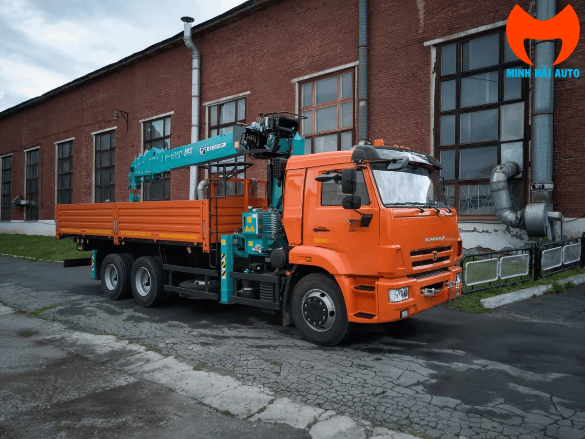 Xe tải KAMAZ cabin cam gắn cẩu Everdigm HLC-8027 đỗ cạnh nhà xưởng gạch đỏ, cần cẩu thu gọn nằm trên thùng