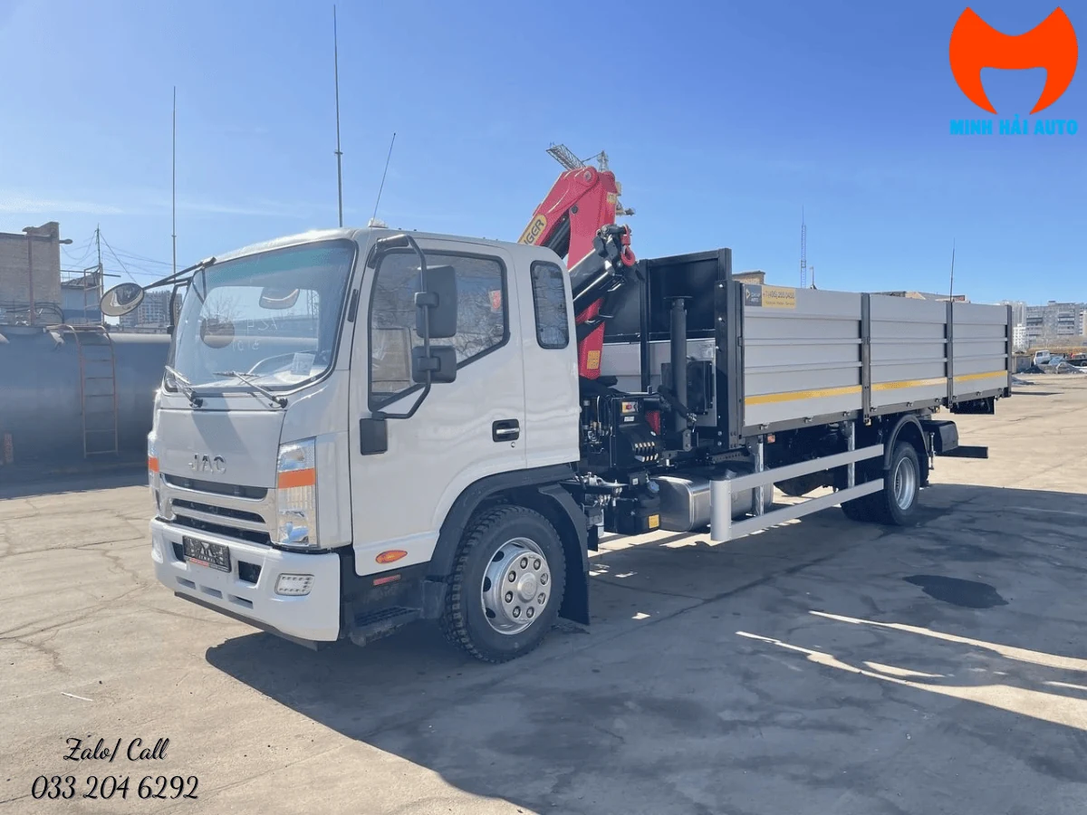 Xe tải JAC gắn cẩu gập Palfinger chụp góc trước chếch trái, cần cẩu gập gọn phía sau ca-bin, xe đỗ tại sân bãi