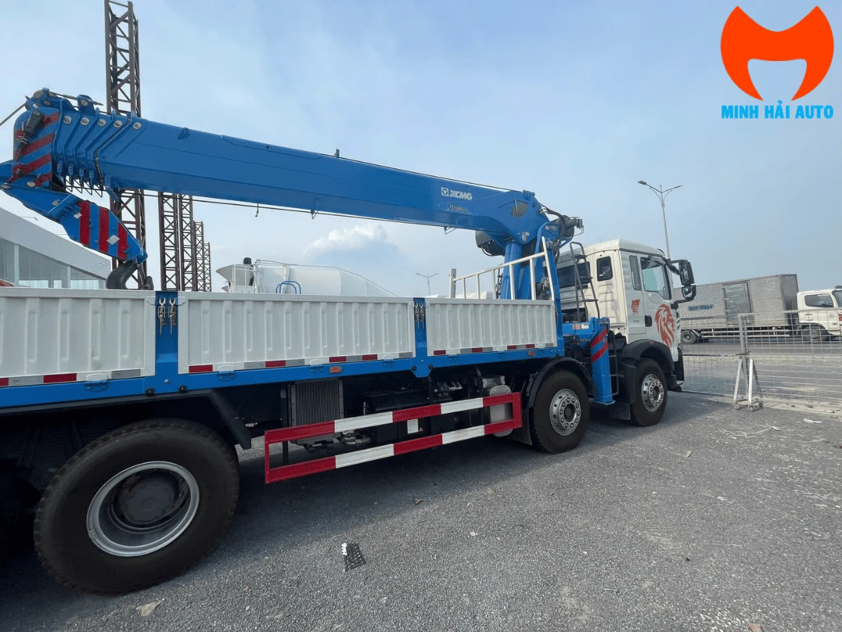 Xe tải Howo bốn chân gắn cẩu XCMG màu xanh dương, nhãn XCMG đọc rõ trên thân cần, thùng lửng trắng xanh