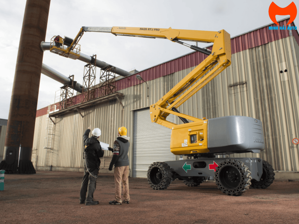 Cần gấp khúc của xe nâng người Haulotte 26m vươn cao qua chướng ngại vật để tiếp cận vị trí làm việc.